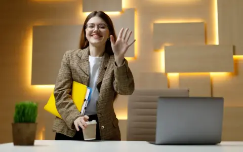 Uśmiechnięta kobieta w okularach macha ręką, trzymając teczkę i kawę. Czy dzień próbny jest płatny?