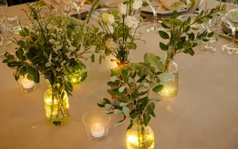 Elegante decoracion con velas y flores en jarrones de cristal, creando un ambiente cálido y acogedor para una cena especial.