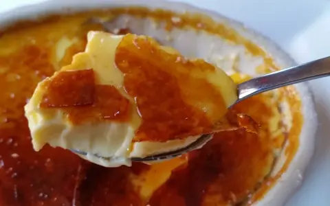 En sked tar en bit av en krämig creme brulee med karamelliserat socker. Perfekt dryck till creme brulee.