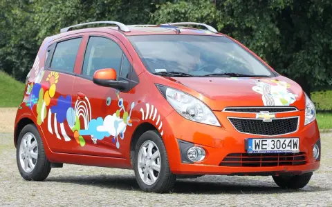 Pomarańczowy Chevrolet Spark z kolorowymi, abstrakcyjnymi wzorami na karoserii.
