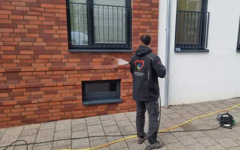 Mann reinigt mit Hochdruckreiniger die Ziegel-Fassade.