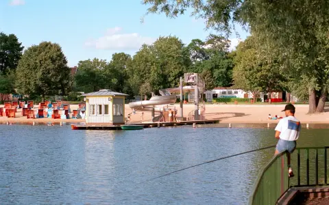 Am Orankesee Strandbad tummeln sich Badegäste, während ein Angler geduldig auf seinen Fang wartet.