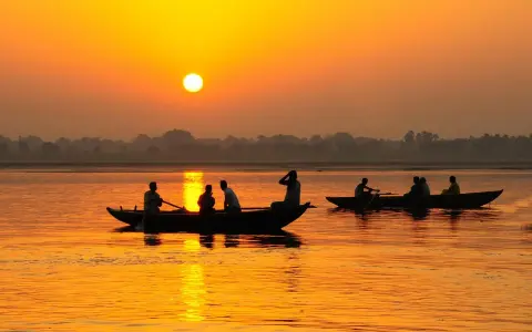 Łodzie na rzece Ganges podczas zachodu słońca. Ludzie płyną łodziami po wodzie, odbijając się w pomarańczowym blasku.