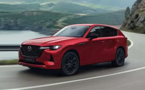 Czerwona Mazda CX-60 3.3 Diesel pokonuje zakręt na malowniczej drodze.