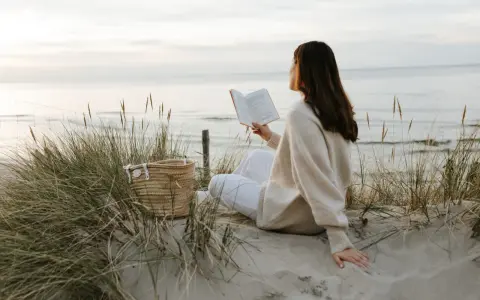 Kobieta czyta książkę na plaży, ciesząc się spokojem i świeżym powietrzem. To idealny moment, by poczuć, kiedy jest najwięcej jodu nad morzem.
