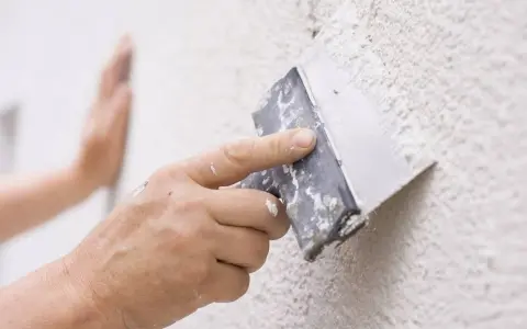 Mano aplicando masa con espátula para reparar gotele en pared.