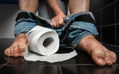 En person sitter på en toalett med neddragna jeans. En rulle toalettpapper ligger bredvid. Tänk på vaccin mot turistdiarré för en tryggare resa.