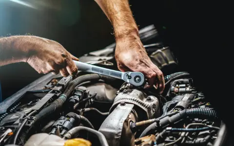 Mechanik dokręca śrubę kluczem w silniku samochodu. Widać jego dłonie i fragmenty silnika, być może podczas rutynowej kontroli lub naprawy.