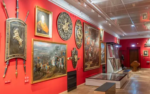 Wnętrze jednego z muzeów w Krakowie. Czerwone ściany zdobią obrazy batalistyczne, portrety i historyczne tarcze.