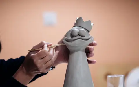 Manos trabajando con arcilla para crear una figura de rana con corona.
