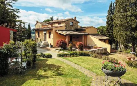 Un perfetto weekend in Toscana: villa con giardino fiorito, cipressi e un cielo azzurro con nuvole bianche.