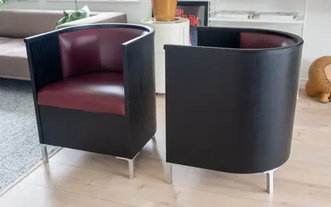 Två svarta fåtöljer med vinröda sitsar, designade av Mats Theselius, står på ett ljust trägolv.