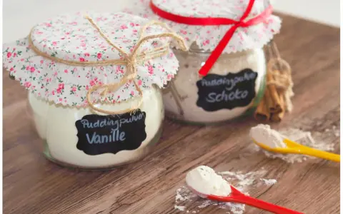 Zwei Gläser mit selbstgemachtem Puddingpulver (Vanille & Schoko) auf einem Holztisch, bereit für köstliche Desserts.