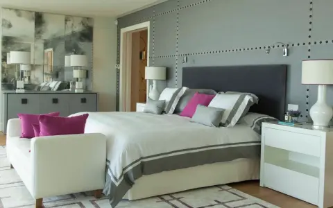 Ideas para diseñar tu habitacion: cama moderna con detalles grises y rosas, mesitas blancas, sofá y espejo decorativo.