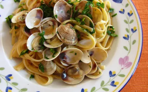 Pyszne spaghetti vongole z małżami i natką pietruszki na talerzu z kwiatowym wzorem.