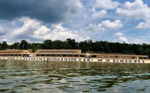 Das Strandbad Wannsee mit seiner langen Promenade und vielen Liegestühlen, im Hintergrund grüne Bäume und ein bewölkter Himmel.