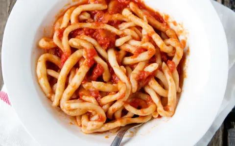 Piatto di pici fatti in casa conditi con un sugo rosso.