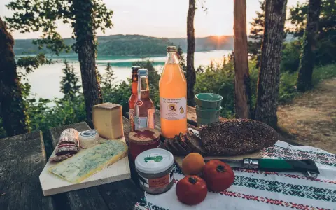 Pique-nique avec fromages, pain de campagne, jus de poire et terrine, un aperçu des spécialités culinaires Jura au bord d'un lac.