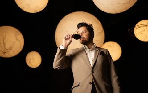Un homme en costume déguste un verre de vin rouge, entouré de lumières rondes évoquant des planètes. Une dégustation qui rappelle la philosophie du vin biodynamique.