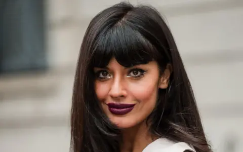 Frau mit leichter Pony und langen, dunklen Haaren, auffälligem Make-up und dunklem Lippenstift.