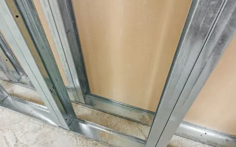 Metalowe profile na ścianki działowe tworzą szkielet konstrukcji. Widać je w zbliżeniu, z płytą gipsowo-kartonową w tle.