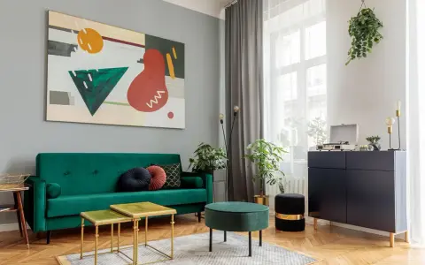 Soggiorno moderno con divano verde smeraldo e tavolini dorati. L'arte astratta sul muro grigio e i mobili scuri creano un perfetto abbinamento colori pareti e mobili.