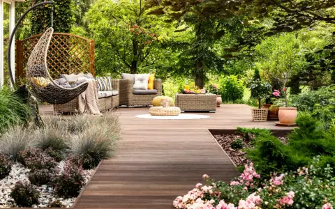 Un rincón acogedor con muebles de mimbre, una hamaca colgante y flores, ideal para disfrutar de pequeños jardines.