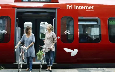 Zwei Frauen mit Fahrrädern steigen in einen roten **denmark train** nach Kopenhagen.