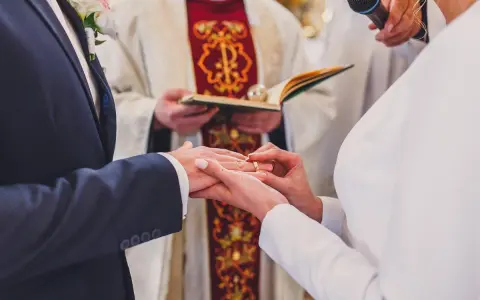 Ceremonia ślubna w kościele. Młoda para wymienia obrączki. W tle ksiądz z księgą. Warto wiedzieć, ile kosztuje ślub kościelny.