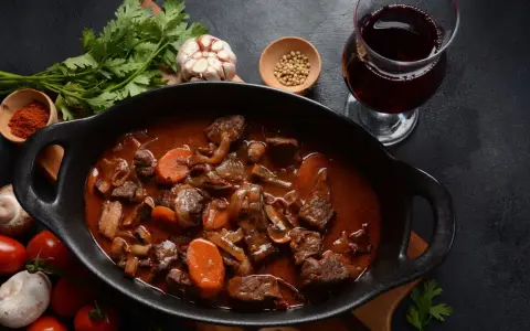 Un plat de vin avec bœuf bourguignon mijoté, garni de carottes et champignons, accompagné d'un verre de vin rouge.