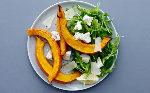 En härlig sallad med ruccola och fetaost, toppad med ugnsrostad pumpa och en citronskiva.