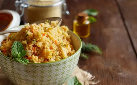 Schüssel mit buntem Couscous, garniert mit Minze. Daneben ein Glas Couscous und eine kleine Flasche Öl. Ein köstlicher Couscous-Baby-Genuss!