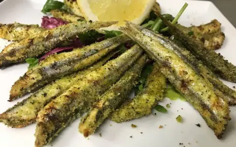 Sardoncini alla romagnola dorati e croccanti, serviti su un letto di insalata fresca con una fetta di limone.