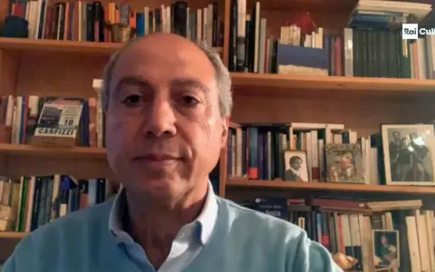 Carmine Abate, con libreria alle spalle, parla in videochiamata.