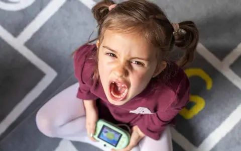 Niña con expresión de enfado y consola de videojuegos, un ejemplo de comportamiento disruptivo significado.