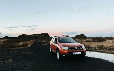 Pomarańczowy samochód na czarnej, wulkanicznej drodze. Islandia oferuje malownicze krajobrazy i swobodny ruch drogowy.