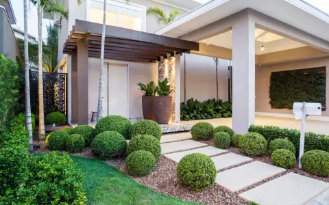 Vialetti giardino moderni con siepi sferiche e un pergolato in legno creano un percorso accogliente verso la casa.