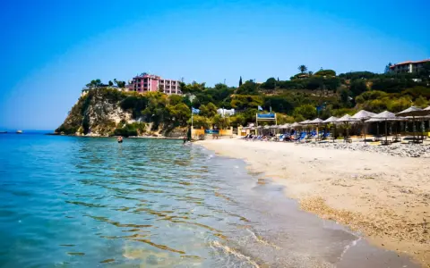 Piękne, turkusowe morze na Zakynthos. Plaża z leżakami i parasolami, a na klifie hotel.