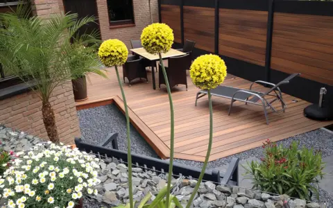 Giardino moderno senza erba: deck in legno, ghiaia, piante in vaso e fiori bianchi. Esempi idee giardino senza erba.