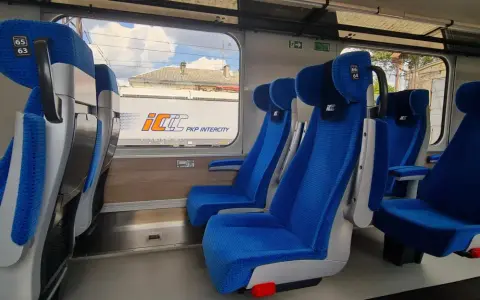 Wygodne, niebieskie fotele w wagonach PKP Intercity bez przedziałów. Widok na mijany krajobraz i inne wagony.