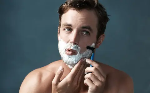 Hombre con espuma de afeitar en la cara, aprendiendo como afeitarse la barba con una maquinilla.
