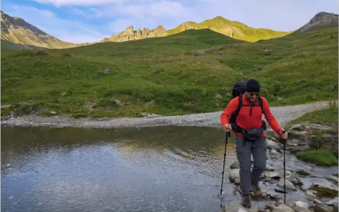 Un randonneur traverse un ruisseau de montagne, bâtons en main. Une belle illustration de pourquoi marcher avec des bâtons pour plus de stabilité.