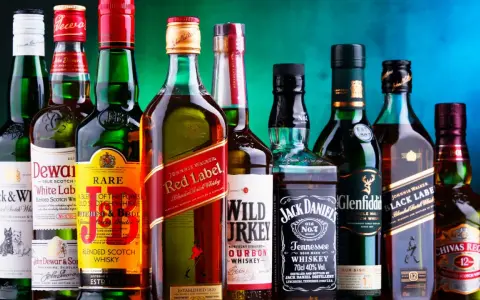 Eine Reihe von Whiskyflaschen, darunter Johnnie Walker Red Label, Jack Daniel's und Chivas Regal. Die Frage "wie viel prozent hat whisky" wird durch die 40% Vol. auf der Jack Daniel's Flasche beantwortet.