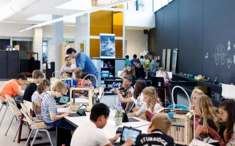 Children engage in 3d printing education, working with laptops and 3D printers in a bright, modern classroom.