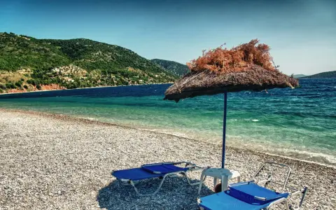 Plaża z leżakami i parasolem, w tle zielone wzgórza i turkusowe morze. To idealne miejsce na wypoczynek na grupie wysp na Morzu Egejskim.