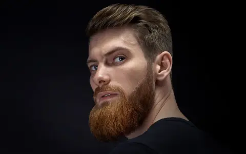 Hombre con barba rojiza y peinado actual, con el pelo peinado hacia atrás y un corte moderno.