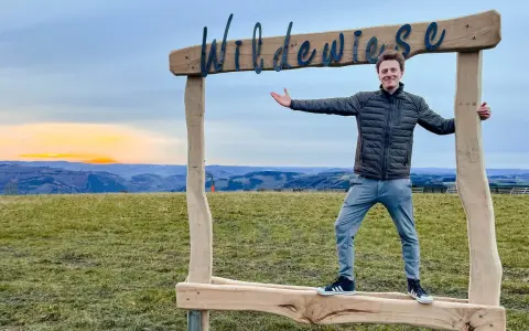 Ein Mann steht vor einem Holzrahmen mit der Aufschrift "Wildewiese". Ein toller Ort für fotospots nrw bei Sonnenuntergang.