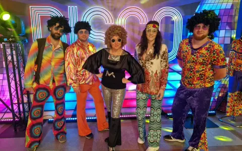 Pięć osób w kolorowych strojach disco z lat 70. na tle napisu "DISCO".