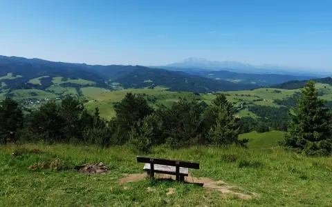 Ławka na przełęczy pod Tokarnią zaprasza do podziwiania malowniczego krajobrazu zielonych wzgórz i odległych gór.