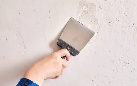 Mano con espátula arreglando una pared con imperfecciones. Aprende como alisar paredes con imperfecciones para un acabado perfecto.